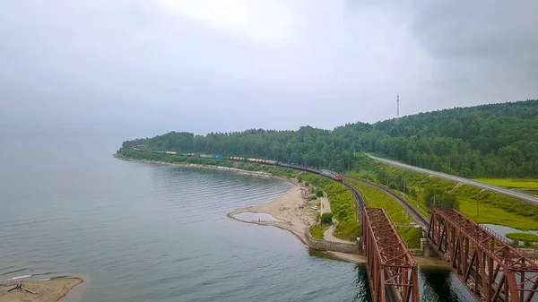 Trans-Siberian Railway, the coast of Lake Baikal. Movement of trains on the iron bridge across the river flowing into Baikal. Russia, From Drone