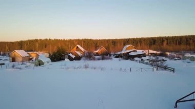 Köyün üzerinde uçan ve kar kaplı tarlalar. gün batımı zamanı. Kışın temiz hava. Video. UltraHD (4k)