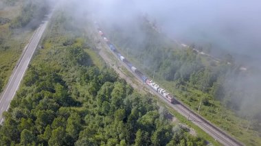 Tren kıyı boyunca bulutlar altında trenle seyahat eder. Transibir demiryolu. Bulutların üstünde uçan. Sahil, Deniz Baykal, dron üzerinden 