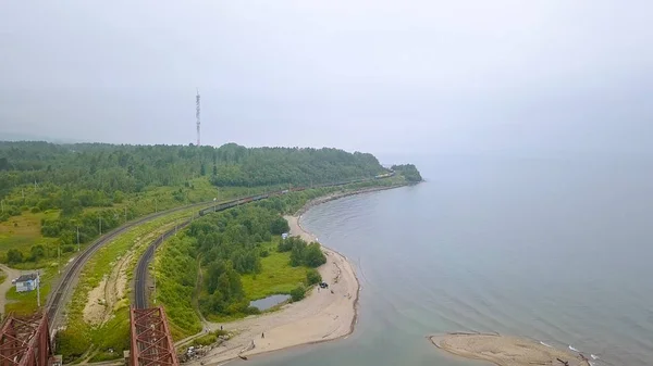 Russia, Baikal - 02 agosto 2018: Ferrovia Transiberiana, la costa del lago Baikal. Movimento dei treni sul ponte di ferro attraverso il fiume che scorre in Baikal, Da Drone — Foto Stock