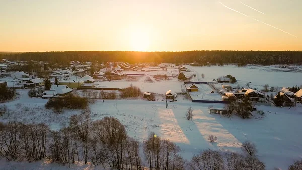 雪に覆われた湖から雪に覆われた村に飛んでいく。冬晴天、夕日バックライト, ドローンから — ストック写真