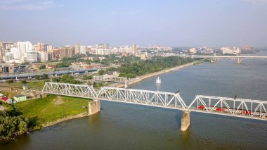 Elektrikli tren Ob nehir geçiyor. Novosibirsk ilk demiryolu köprüsü. Novosibirsk şehir panoraması. Rusya'dan Dron 
