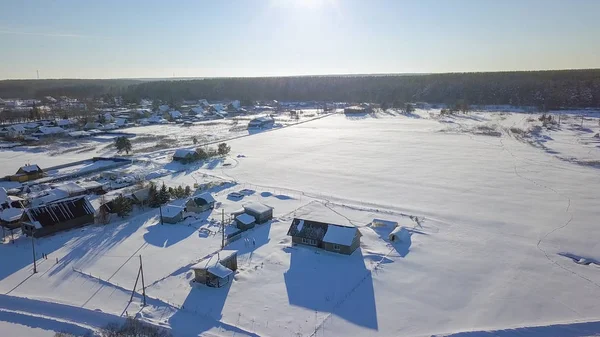Voando sobre a aldeia e campos cobertos de neve contra o sol. As hélices de drones são visíveis. Hora da noite. Inverno tempo claro, a partir de Drone — Fotografia de Stock