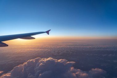 Havada, uçak penceresinden görüntülenen, koyu mavi gökyüzü ufku ve güneş doğma süresi bulut arka plan ile uçak kanat siluetgörünümü