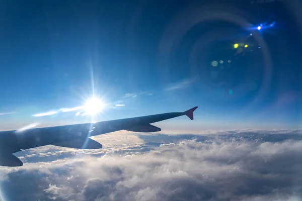 Up in the air, view of aircraft wing silhouette in dark blue sky horizon and cloud background in sun rise time. viewed from airplane window, with a reflection camera lens