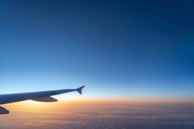 Havada, uçak penceresinden görüntülenen, koyu mavi gökyüzü ufku ve güneş doğma süresi bulut arka plan ile uçak kanat siluetgörünümü
