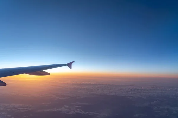 Up in the air, view of aircraft wing silhouette with dark blue sky horizon and cloud background in sun rise time, viewed from airplane window