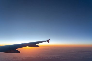 Havada, uçak penceresinden görüntülenen, koyu mavi gökyüzü ufku ve güneş doğma süresi bulut arka plan ile uçak kanat siluetgörünümü