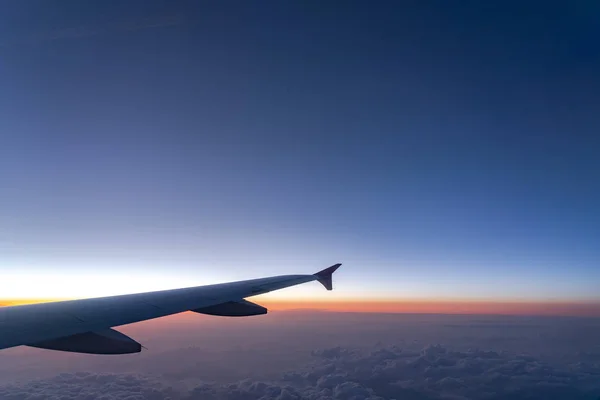 Up in the air, view of aircraft wing silhouette with dark blue sky horizon and cloud background in sun rise time, viewed from airplane window — Stock Photo, Image