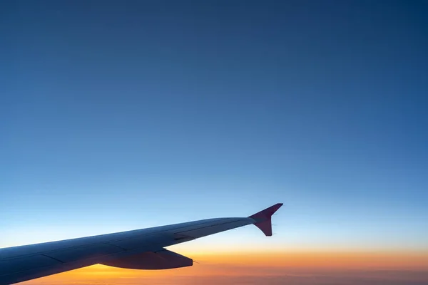 Up in the air, view of aircraft wing silhouette with dark blue sky horizon and cloud background in sun rise time, viewed from airplane window