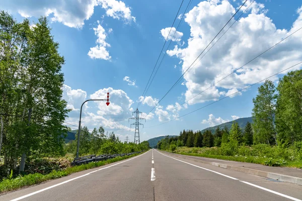 Γραμμές ισχύος μεταφοράς ηλεκτρισμού Πύργος υψηλής τάσης σε πράσινη φύση ατέλειωτος ασφαλτοστρωμένος δρόμος σε μια αγροτική περιοχή. μπλε ουρανό λευκό σύννεφα φόντο το καλοκαίρι ηλιόλουστη μέρα — Φωτογραφία Αρχείου