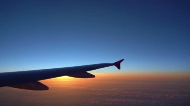 Havada, uçak penceresinden görüntülenen, koyu mavi gökyüzü ufku ve güneş doğma süresi bulut arka plan ile uçak kanat siluetgörünümü
