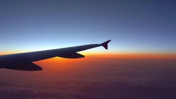 在空中 从飞机窗口看 在太阳升起时 有深蓝色天空地平线和云背景的飞机机翼剪影 — 图库视频影像