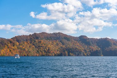 Lake Towada Gezi Turları. Güzel görünümü, berrak mavi gökyüzü, beyaz bulut, sonbahar yeşillik sezon arka plan ile güneşli bir günde yolcu gemisi. Aomori, Japonya. Gemide Japonca Metin 