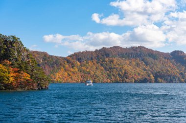 Lake Towada Gezi Turları. Güzel görünümü, berrak mavi gökyüzü, beyaz bulut, sonbahar yeşillik sezon arka plan ile güneşli bir günde yolcu gemisi. Aomori, Japonya. Gemide Japonca Metin 