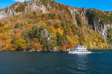 Lake Towada Gezi Turları. Güzel görünümü, berrak mavi gökyüzü, beyaz bulut, sonbahar yeşillik sezon arka plan ile güneşli bir günde yolcu gemisi. Aomori, Japonya. Gemide Japonca Metin 