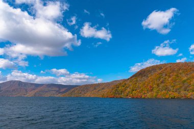 Güzel sonbahar yeşillik manzara manzaralar. Sonbahar muhteşem renklerle doludur. Towada Gölü kıyısından görünümü, berrak mavi gökyüzü ve su, beyaz bulut, güneşli gün arka plan. Aomori Prefecture, Japonya