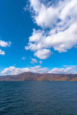 Güzel sonbahar yeşillik manzara manzaralar. Sonbahar muhteşem renklerle doludur. Towada Gölü gezi Cruise gemi görünümü. Berrak mavi gökyüzü, su, beyaz bulut, güneşli bir gün arka plan. Aomori, Japonya