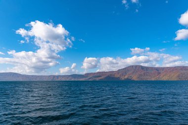 Güzel sonbahar yeşillik manzara manzaralar. Sonbahar muhteşem renklerle doludur. Towada Gölü gezi Cruise gemi görünümü. Berrak mavi gökyüzü, su, beyaz bulut, güneşli bir gün arka plan. Aomori, Japonya
