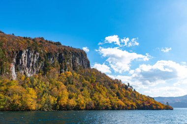 Güzel sonbahar yeşillik manzara manzaralar. Sonbahar muhteşem renklerle doludur. Towada Gölü gezi Cruise gemi görünümü. Berrak mavi gökyüzü, su, beyaz bulut, güneşli bir gün arka plan. Aomori, Japonya