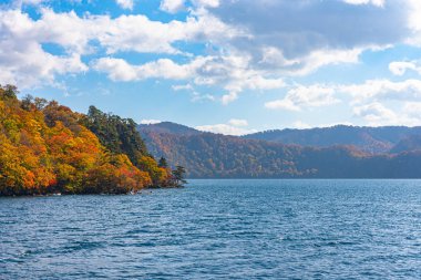 Güzel sonbahar yeşillik manzara manzaralar. Sonbahar muhteşem renklerle doludur. Towada Gölü gezi Cruise gemi görünümü. Berrak mavi gökyüzü, su, beyaz bulut, güneşli bir gün arka plan. Aomori, Japonya