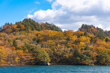 Güzel sonbahar yeşillik manzara manzaralar. Sonbahar muhteşem renklerle doludur. Towada Gölü gezi Cruise gemi görünümü. Berrak mavi gökyüzü, su, beyaz bulut, güneşli bir gün arka plan. Aomori, Japonya