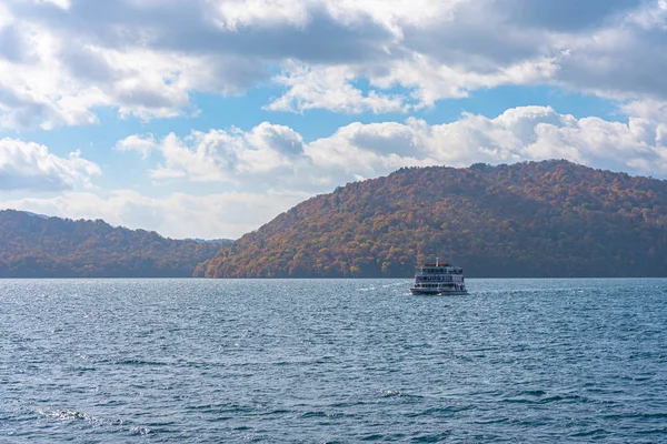 Lake Towada Sightseeing Cruises. Beautiful view, clear blue sky, white cloud, cruise ship in sunny day with autumn foliage season background. Aomori, Japan. Text in Japanese on ship \