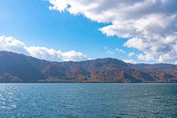 Beautiful autumn foliage scenery landscapes. Fall is full of magnificent colors. View from Lake Towada sightseeing Cruise ship. Clear blue sky, water, white cloud, sunny day background. Aomori, Japan — Stock Photo, Image