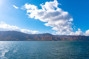 Güzel sonbahar yeşillik manzara manzaralar. Sonbahar muhteşem renklerle doludur. Towada Gölü gezi Cruise gemi görünümü. Berrak mavi gökyüzü, su, beyaz bulut, güneşli bir gün arka plan. Aomori, Japonya