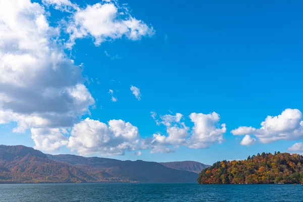 Beautiful autumn foliage scenery landscapes. Fall is full of magnificent colors. View from Lake Towada sightseeing Cruise ship. Clear blue sky, water, white cloud, sunny day background. Aomori, Japan — Stock Photo, Image