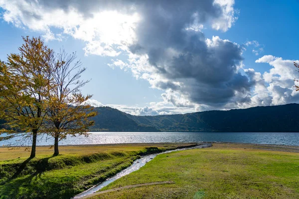 Beautiful autumn foliage scenery landscapes of Lake Towada in sunny day. View from lakeside, clear sky, blue water and white cloud in the background. Towada Hachimantai National Park, Aomori, Japan — Stock Photo, Image