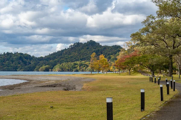 Beautiful autumn foliage scenery landscapes of Lake Towada in sunny day. View from lakeside, clear sky, blue water and white cloud in the background. Towada Hachimantai National Park, Aomori, Japan — Stock Photo, Image