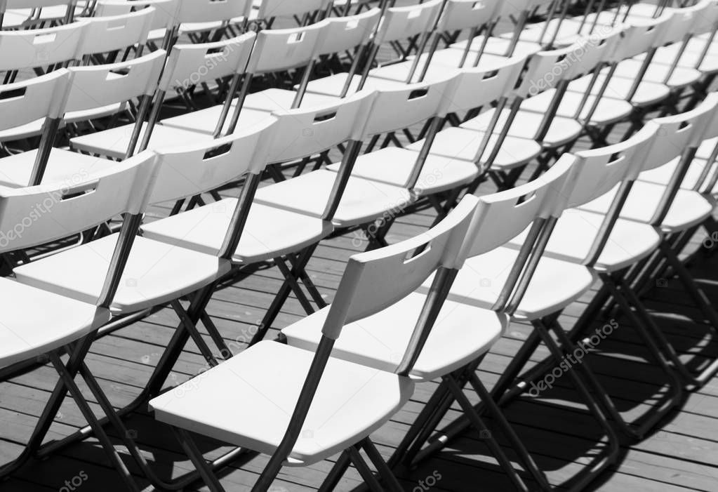 Rows of white empty folding chairs in a summer theatre.
