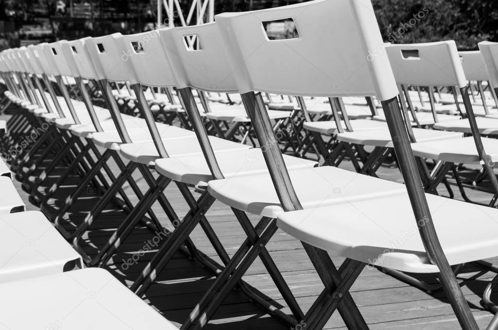 minimalistic picture of rows of white empty folding chairs in a summer theatre.