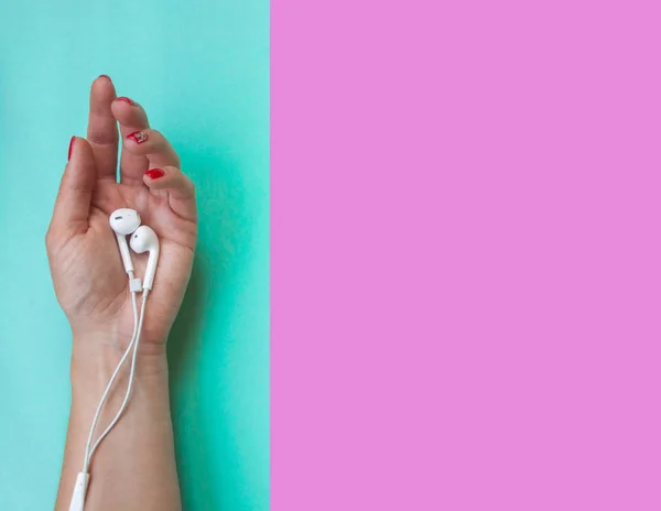 Ladys mão segurando fones de ouvido em turquesa e rosa quartzo cor de fundo . — Fotografia de Stock