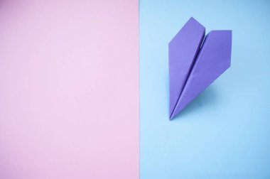 Düz metin alanı ile mor kağıt uçak pastel pembe ve mavi zemin üzerinde yatıyordu.