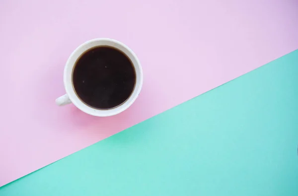 A cup of fresh black coffee on pink and green background with text space.