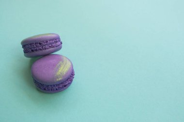 İki güzel ve lezzetli mor macaroons Altın vuruş metin alanı ile mavi arka plan ile renk.