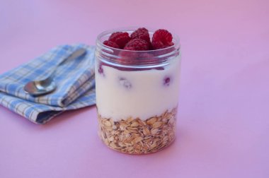 Granola taze tatlı ahududu mavi renk peçete üzerinde pembe bir arka plan üzerinde bir cam kavanoza, yakın çekim.