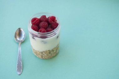 Granola taze tatlı ahududu ve bir kaşık ile güzel cam kavanozda üstten görünüm mavi zemin üzerine.