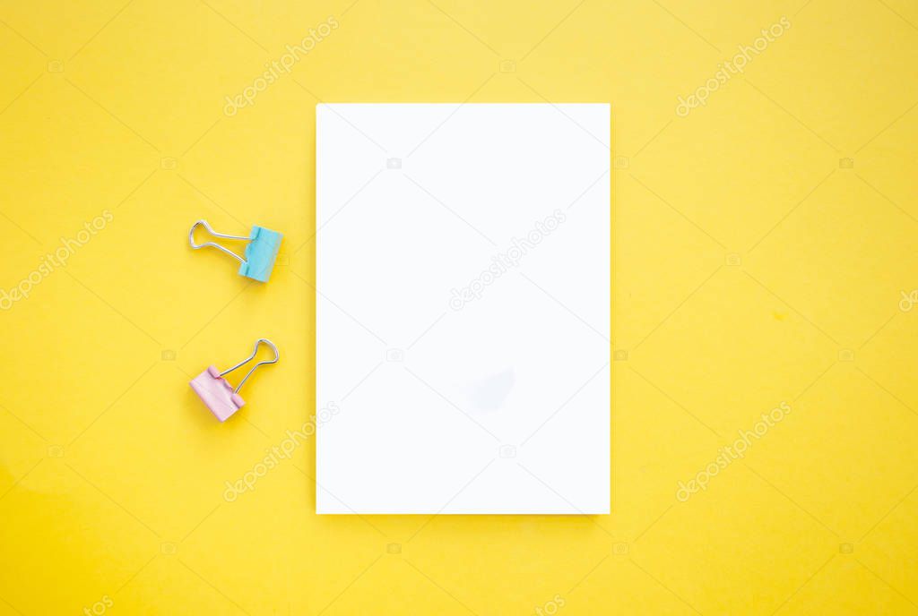 Notepad and binder clips on bright yellow background with copyspace. Back to school concept.