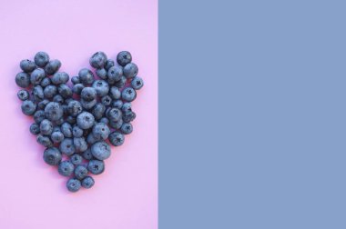 Lezzetli taze çekilmiş bluberry boşaltmak ile mor ve pembe arka plan üzerinde kalp şeklinde. Sağlıklı gıda kavramı.