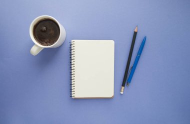 Not defteri, kalem, bir fincan kahve mor zemin üzerine.