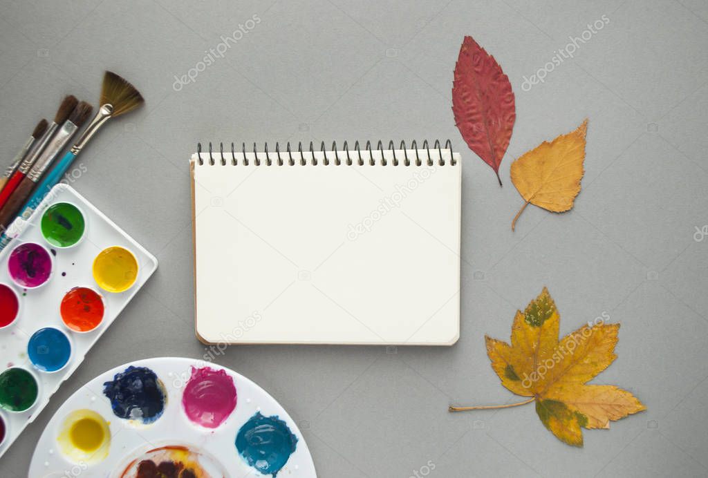 Flat lay of watercolor palette, paint brushes, notepad and autumn leaves. Hello autumn concept.