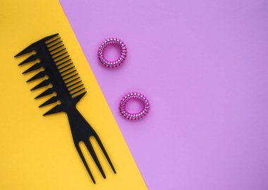 Siyah plastik tarak ve pastel pembe ve sarı zemin üzerine iki pembe parlak scrunchies.