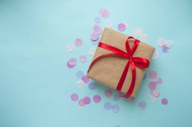 Hediye kutusu kahverengi renkli Kraft kağıt sarılı ve colofrul konfeti ve boşaltmak mavi zemin üzerine kırmızı yay ile bağlı.