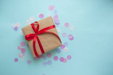 Hediye kutusu pastel mavi zemin üzerine kırmızı kurdele ile bağlanmış.
