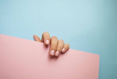 Genç kadının güzel manikür pembe renkli kağıt üzerinde mavi arka plan ile boşaltmak arkasına saklanmış ile el.