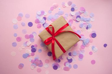 Hediye kutusu pastel pembe bir arka plan üzerinde kırmızı kurdele ile bağlanmış.