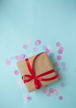 Hediye kutusu pastel mavi zemin üzerine kırmızı kurdele ile bağlanmış.